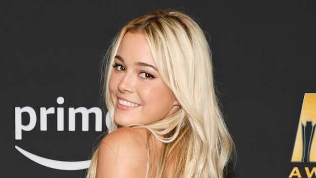 Olivia Dunne poses and smiles over her shoulder at the camera. She wears her blond hair down in a light wave.